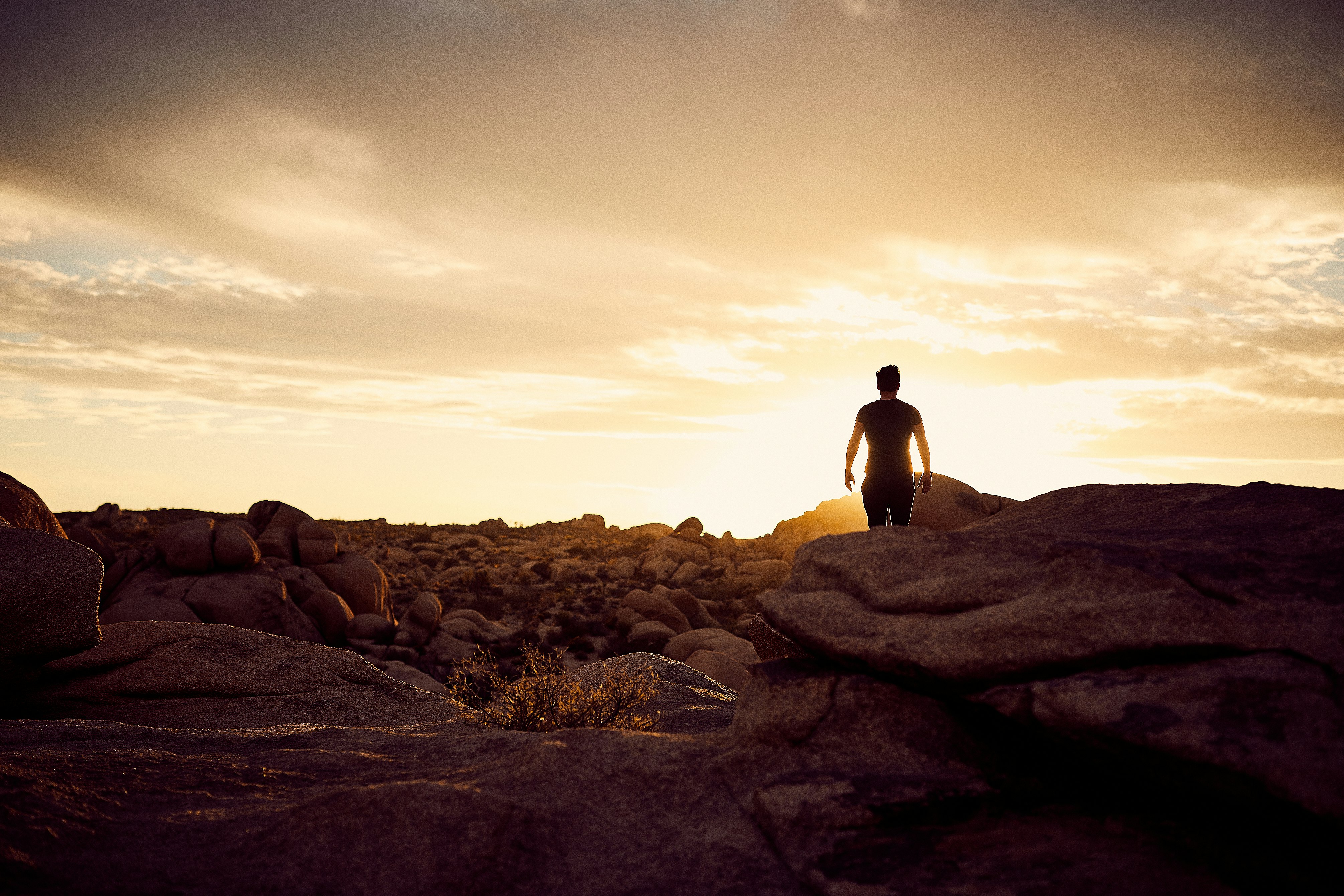 man walking on gray rocks under yellow sky during daytime